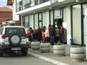 Voters queueing in front of a polling station and an OSCE vehicle.JPG